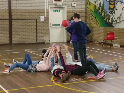 kids in school gym lying on floor with arms and a ball above